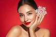 © Oleg Gekman - Beautiful young woman with red lipstick, shiny clean skin and face, showing glowing snowflake, near face and smiling, isolated on a red background. Christmas holidays concept