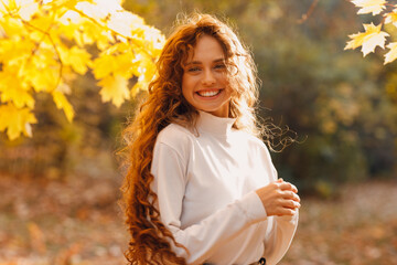 Wall Mural - Smiling young woman enjoy the autumn weather in the parkland with the yellow leaves at branches