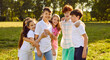 © Studio Romantic - Portrait of happy smiling children friends standing on the green grass together in the park outdoors and looking cheerful at the camera hugging and having fun. Kids summer camp and holidays concept.