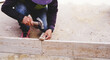 Construction builder worker uses a hammer to driving iron nail into a wooden beam at building site for guideline frame to filling formwork with wet concrete to build concrete floor on the work area.