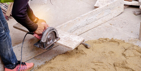 Construction builder worker uses a circular saw to cut wood at building site for preparation to build concrete floor on the work area.