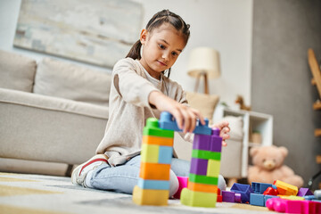 Wall Mural - cute girl playing with colorful toy blocks on carpet in modern living room, building tower game