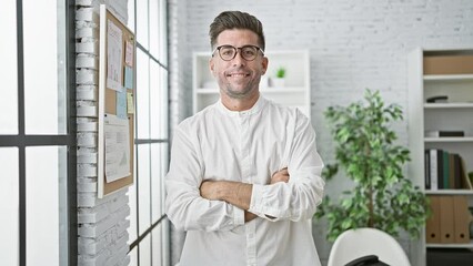 Wall Mural - Smiling young hispanic man exuding confidence at the office, standing with arms crossed