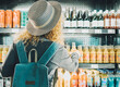 Back view of woman tourist with backpack in front of a window store full of drinks bottles choosing one to buy and drink. Concept of travel solo female people in front of an automatic machine