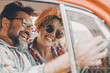 © simona - Happy couple having fun inside a car during travel adventure. Cheerful man and woman smiling and laughing a lot together. People enjoying vehicle trip in friendship and relationship. Concept of drive