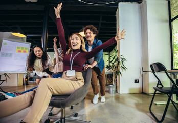 Wall Mural - Young cheerful businesspeople in smart casual wear having fun while racing on office chairs and smiling