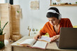 © LIGHTFIELD STUDIOS - concentrated short haired woman with headphones studying from home looking at textbook, education