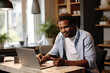 © AI_images - African American male entrepreneur talking over mobile phone and looking at camera while working over laptop at home