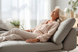 © AI_images - Cheerful sleepy blonde older lady lying on couch