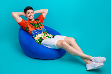 Canvas Print - Full size photo of relaxed guy wear tropical shirt stylish shorts sit on bean bag arms behind head isolated on blue color background