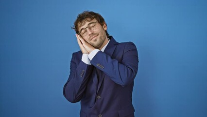 Sticker - Young man wearing business suit sleeping tired dreaming and posing with hands together while smiling with closed eyes. over isolated blue background