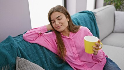 Wall Mural - Young beautiful hispanic woman drinking coffee sitting on sofa at home