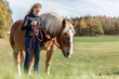 A young woman and her noriker coldblood draught horse on a meadow in autumn outdoors