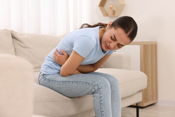 Poster - Woman suffering from abdominal pain on sofa at home. Unhealthy stomach