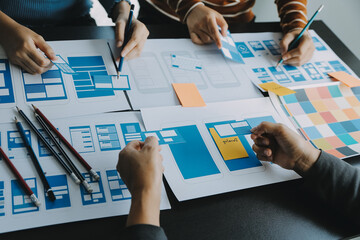 Close up ux developer and ui designer brainstorming about mobile app interface wireframe design on table with customer breif and color code at modern office.Creative digital development agency