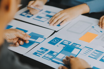 Close up ux developer and ui designer brainstorming about mobile app interface wireframe design on table with customer breif and color code at modern office.Creative digital development agency