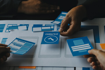 Close up ux developer and ui designer brainstorming about mobile app interface wireframe design on table with customer breif and color code at modern office.Creative digital development agency