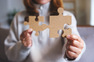 Wall Mural - Closeup image of a woman holding and putting a piece of wooden jigsaw puzzle together