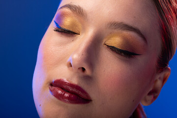 Caucasian woman with brown hair wearing golden eye shadow and red lipstick on blue background