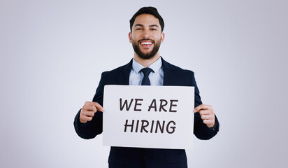 Canvas Print - Happy businessman, portrait and hiring sign for opportunity, advertising or marketing against a gray studio background. Man smile with billboard or poster for recruiting, interview or career position