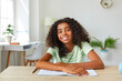 © Studio Romantic - Webcam portrait of smiling dark-skinned schoolgirl who having online class learning at home. Joyful cute curly african american teenage girl with notebook sitting at table in front of web camera.