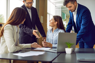 Wall Mural - Team of young business people meeting by office table. Group of male and female employees working together, discussing current affairs, looking at some documents and using laptop computer