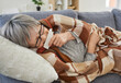 © Studio Romantic - Close up portrait of senior sick woman lying on sofa at home wrapped in a blanket and suffering from runny nose. Elderly female person with seasonal flu feeling unhealthy with influenza.