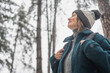 © olezzo - A young mature woman breathes fresh air and enjoys the snowfall in the winter forest. Winter walks and activity concept