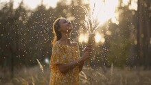 Young Beautiful Woman in yellow dress enjoying sunset in Forest playing with dry fluffy flowers, spikelets, dandelions. cinematic view girl with blowing fluff on summer lawn. Allergy free concept