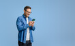 © Moon Safari - Smiling handsome businessman text messaging over mobile phone while standing on blue background