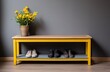 A minimalist interior with a yellow bench, on which there is a flower pot and under it are three pairs of shoes against a grey background.
