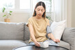 Hypotension problem asian young woman sitting on couch checking blood high pressure and heart rate with digital pressure monitor, making self check up pulse on arm, cuff at home. Healthcare medical.