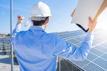 Happy engineer in protective helmet on a solar power plant celebrating success. High quality photo