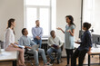© fizkes - Serious African American business team employee making report to colleague on office meeting. Project leader speaking before group. Company teacher training new workers, explaining tasks