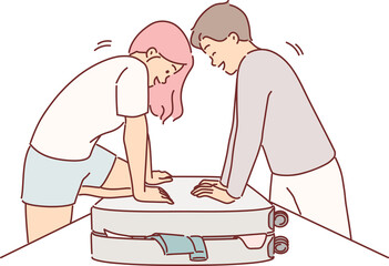 Couple is packing up luggage for travel and trying to close overstuffed suitcase full of clothes