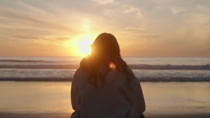 Wall Mural - Footage of a young girl sitting on the beach during a vibrant sunset in the sky