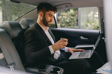 Wall Mural - Professional male finansist working on laptop sitting car backseat and drinking coffee