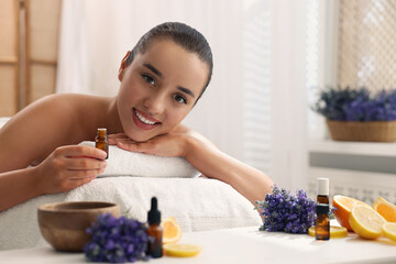 Wall Mural - Beautiful young woman with bottle of essential oil on massage couch in spa salon