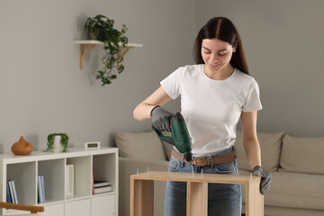 Poster - Young woman with electric screwdriver assembling furniture at home. Space for text