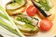 Delicious sandwiches with sprats, pickled cucumber and green onion served with tomato on plate, closeup