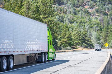 Green industrial carrier big rig semi truck tractor with extended cab for truck driver rest  transporting cargo in reefer semi trailer running on the one way highway road in California mountain range