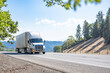 Work horse big rig semi truck transporting cargo in loaded refrigerator semi trailer driving on the mountain highway road in California