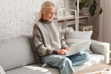 Mature female programmer working with laptop on sofa at home