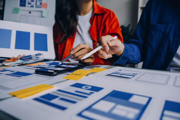 Close up ux developer and ui designer brainstorming about mobile app interface wireframe design on table with customer breif and color code at modern office.Creative digital development agency