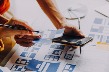 Close up ux developer and ui designer brainstorming about mobile app interface wireframe design on table with customer breif and color code at modern office.Creative digital development agency