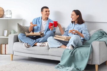 Canvas Print - Young couple with drinks eating tasty pepperoni pizza at home