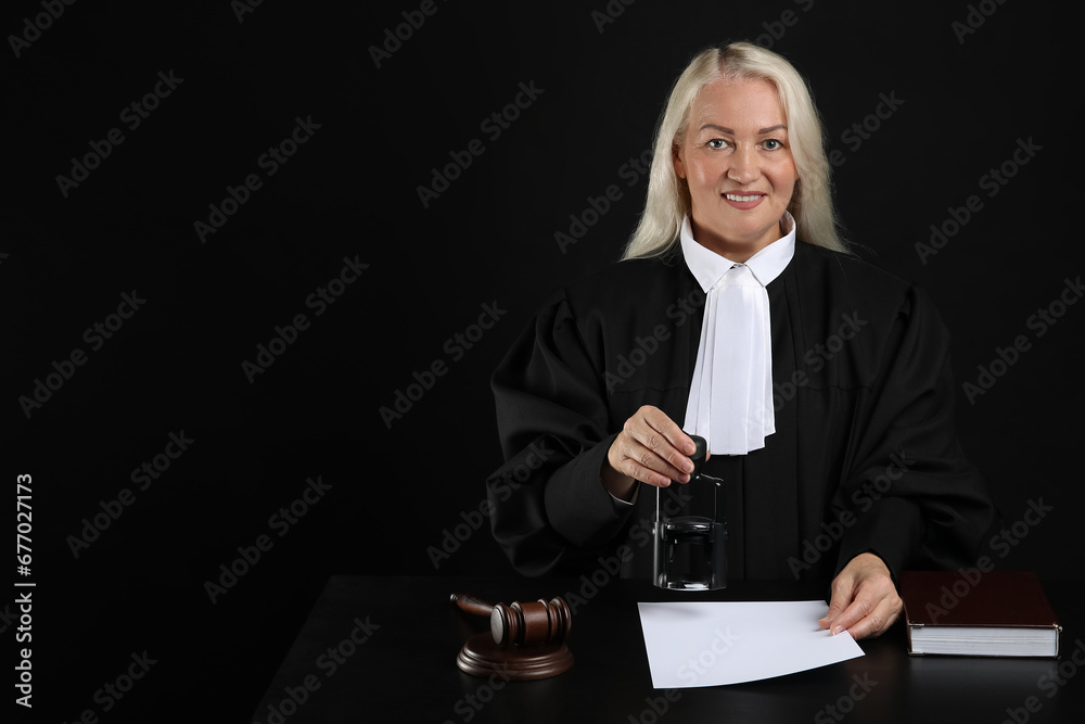 Mature female judge with stamp and document at table on black background