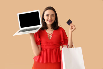 Poster - Young woman with credit card, laptop and shopping bags on beige background