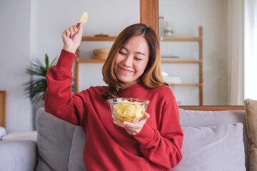 Wall Mural - Portrait image of a young woman picking and eating potato chips at home