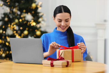 Sticker - Celebrating Christmas online with exchanged by mail presents. Smiling woman opening gift box during video call on laptop at home